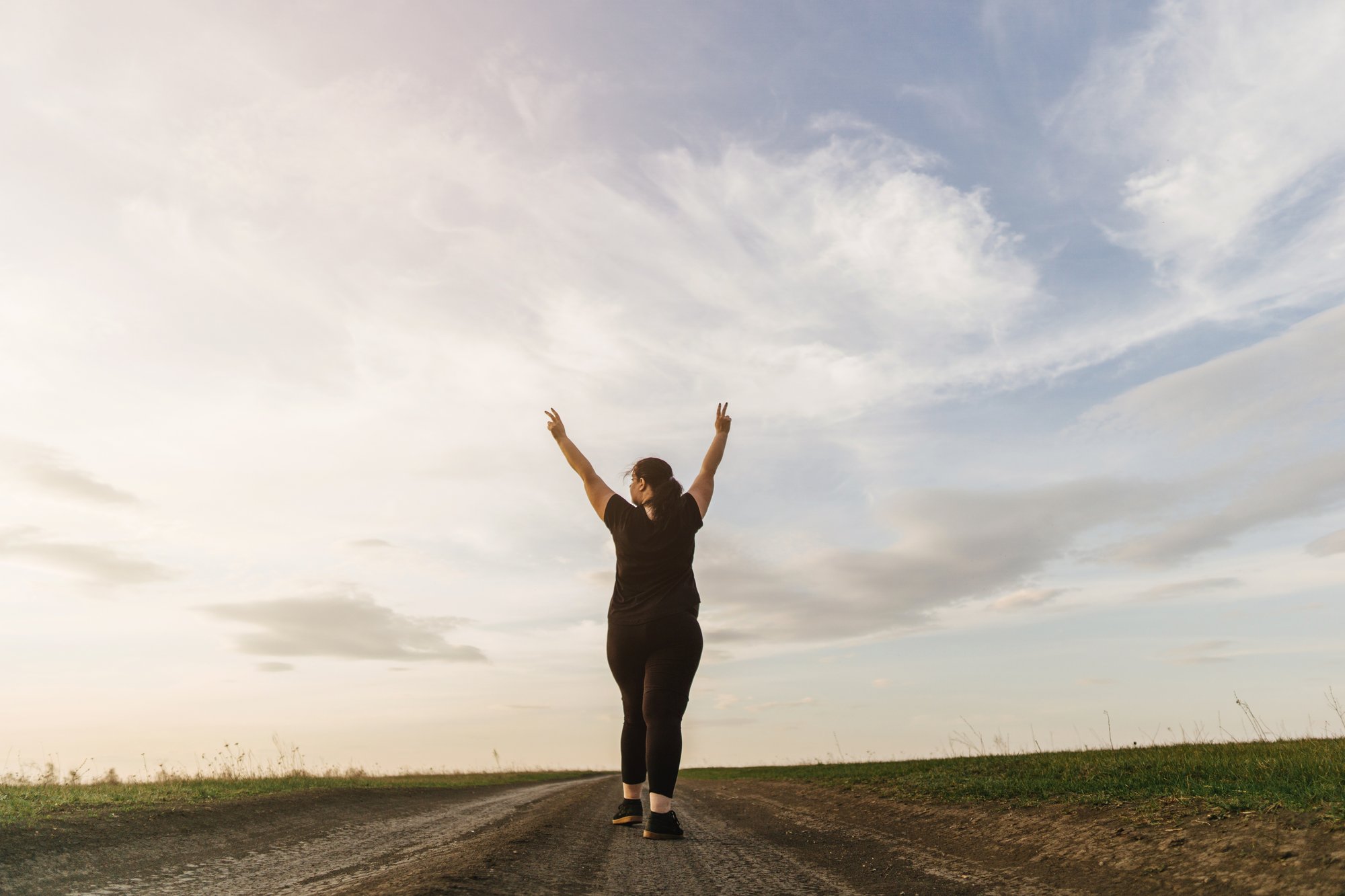 woman walking on straight road with arms in the air